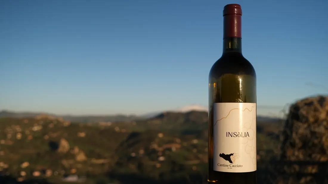 Bottiglia di Insòlia davanti alle colline siciliane al tramonto